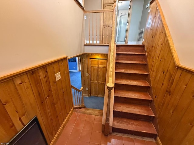 stairway featuring wainscoting, wood walls, visible vents, and tile patterned floors