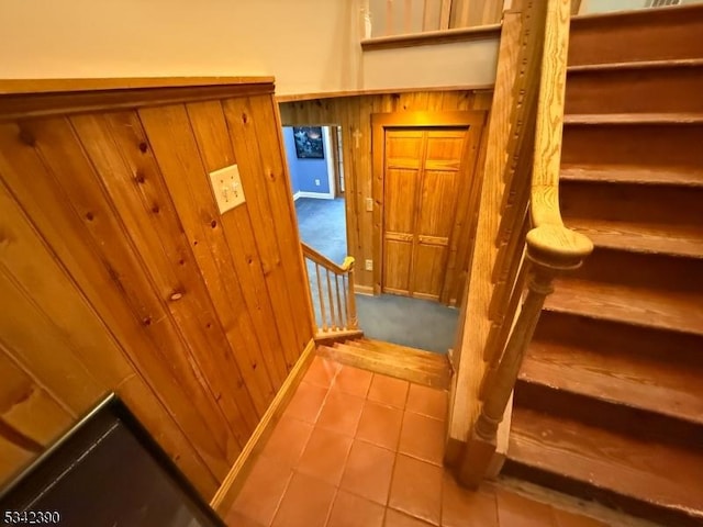 stairs with tile patterned flooring and wood walls