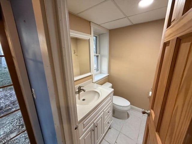 half bath featuring a drop ceiling, tile patterned flooring, toilet, vanity, and baseboards