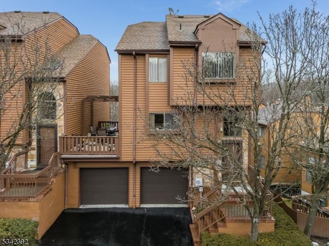 back of property with aphalt driveway, roof with shingles, a balcony, and an attached garage