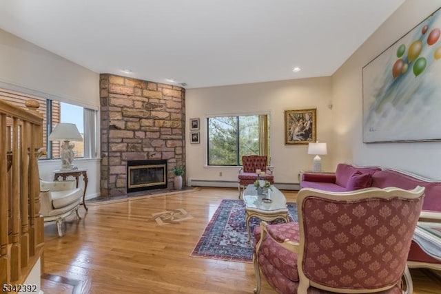 living area with a stone fireplace, a baseboard radiator, and wood finished floors