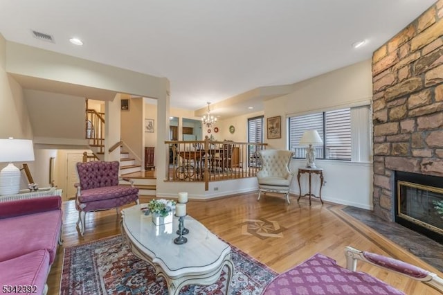 living room featuring a fireplace, visible vents, stairway, wood finished floors, and a chandelier