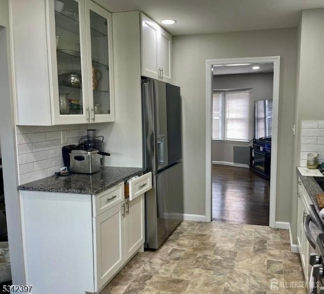 kitchen featuring decorative backsplash, glass insert cabinets, dark stone countertops, black refrigerator with ice dispenser, and white cabinetry