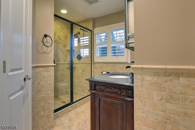 full bath featuring a stall shower, visible vents, a wainscoted wall, vanity, and tile walls