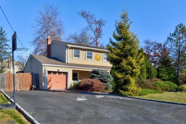 traditional-style home with a garage, driveway, a chimney, fence, and stucco siding