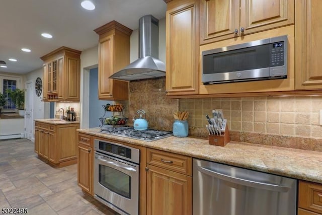 kitchen featuring a sink, appliances with stainless steel finishes, wall chimney range hood, and decorative backsplash