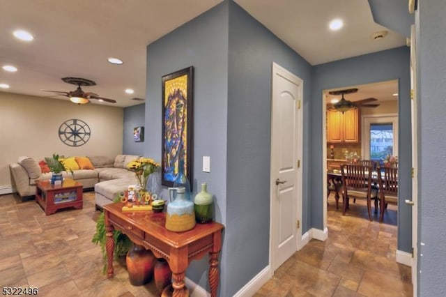 hallway featuring stone finish flooring, baseboards, and recessed lighting