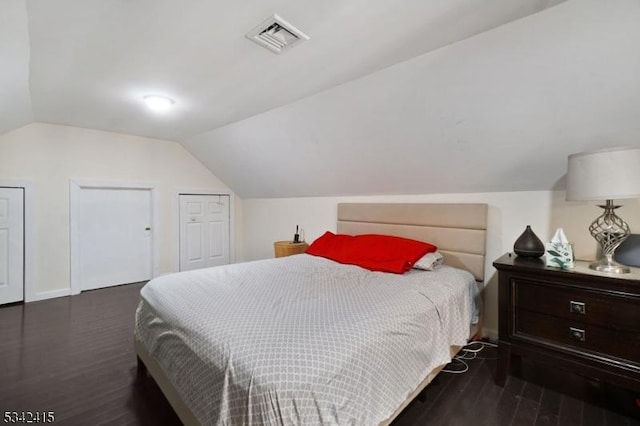 bedroom with visible vents, multiple closets, baseboards, lofted ceiling, and wood finished floors