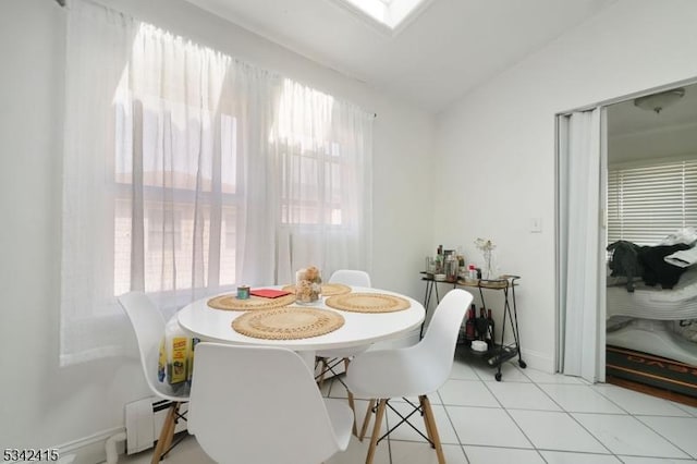 dining area featuring light tile patterned flooring, lofted ceiling with skylight, baseboards, and a baseboard radiator