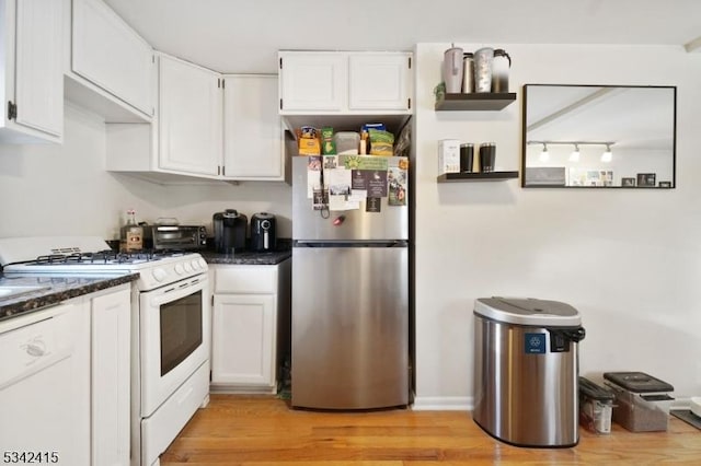 kitchen with white gas range, dark stone countertops, freestanding refrigerator, light wood-style floors, and white cabinetry