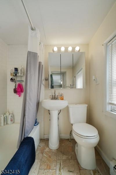 bathroom with a baseboard radiator, baseboards, toilet, and shower / tub combo