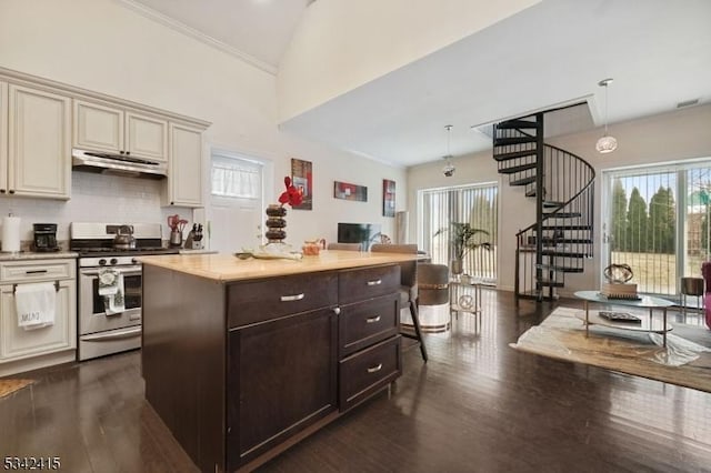 kitchen featuring stainless steel gas range oven, under cabinet range hood, cream cabinets, dark wood finished floors, and light countertops