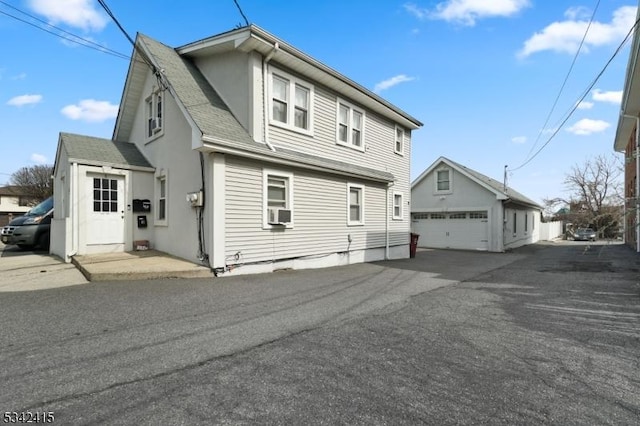 exterior space with an outbuilding, cooling unit, a garage, and roof with shingles