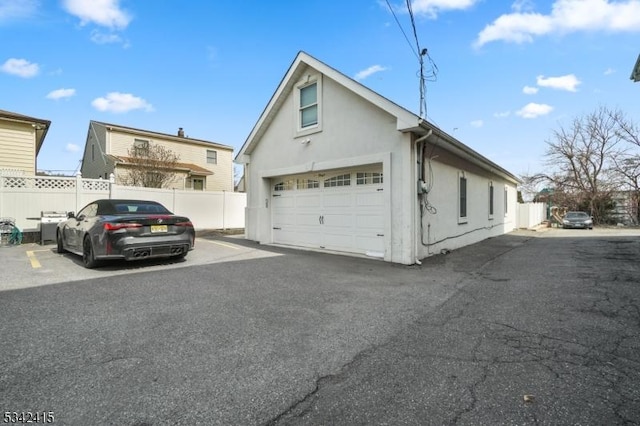 view of property exterior featuring a garage, stucco siding, and fence