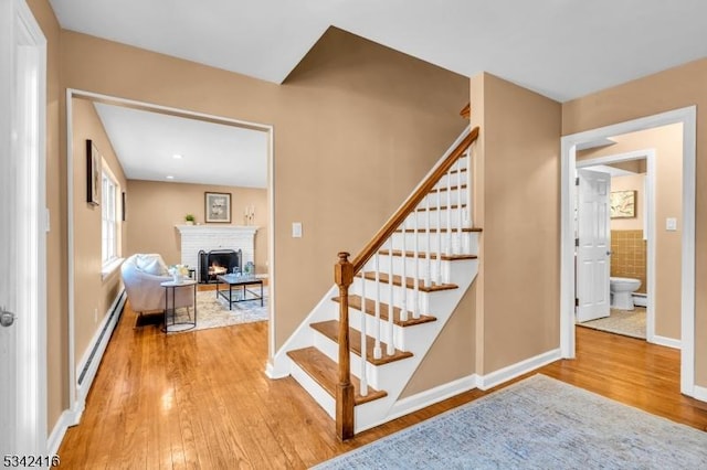 stairway featuring baseboard heating, a brick fireplace, wood finished floors, and baseboards