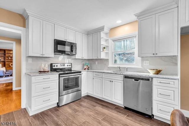 kitchen with white cabinets, wood finished floors, light stone countertops, stainless steel appliances, and a sink