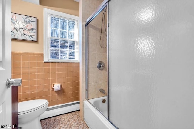 bathroom with toilet, bath / shower combo with glass door, a baseboard radiator, and tile walls