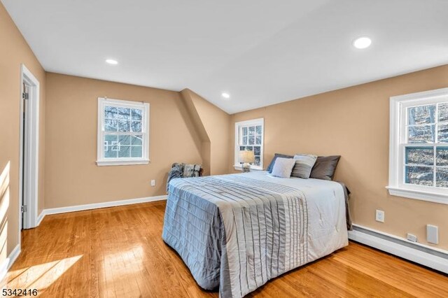 bedroom featuring a baseboard heating unit, multiple windows, baseboards, and wood finished floors