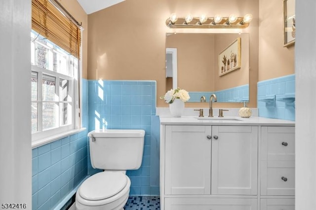 bathroom featuring toilet, wainscoting, vanity, and tile walls