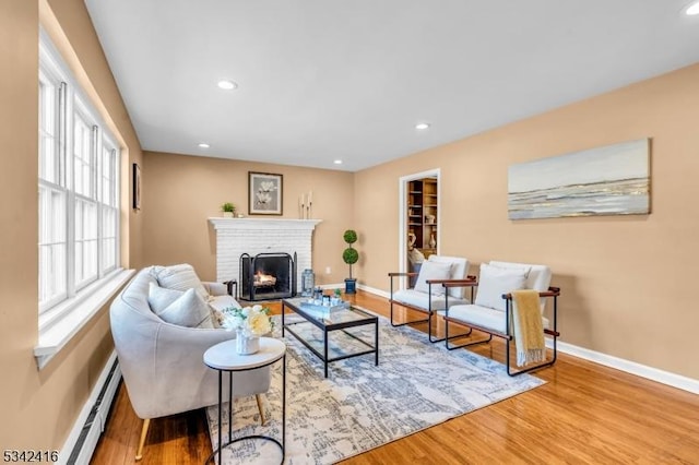 living area featuring a brick fireplace, baseboards, baseboard heating, and wood finished floors