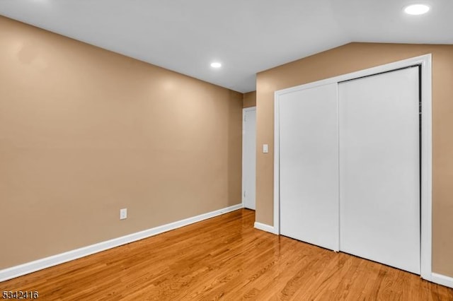 unfurnished bedroom featuring recessed lighting, baseboards, vaulted ceiling, light wood-style floors, and a closet