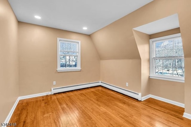 additional living space with a baseboard heating unit, baseboards, vaulted ceiling, and hardwood / wood-style floors