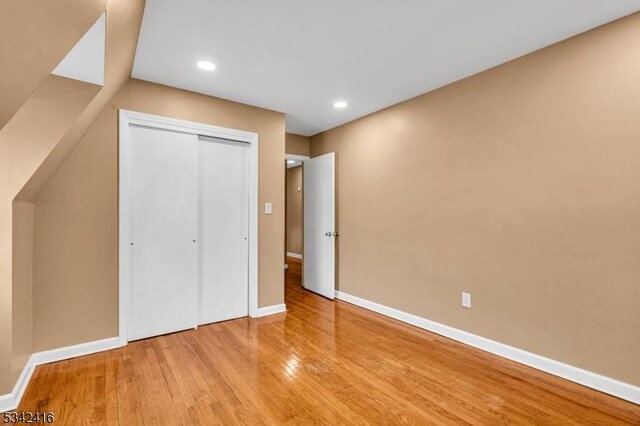 unfurnished bedroom with a closet, recessed lighting, hardwood / wood-style flooring, and baseboards