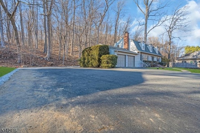 view of home's exterior featuring an attached garage, driveway, a chimney, and fence