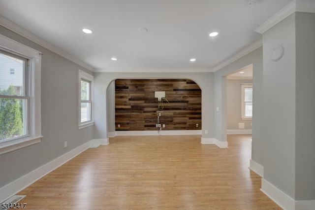 unfurnished living room featuring light wood-style flooring, an accent wall, arched walkways, and ornamental molding