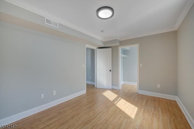 unfurnished room with light wood-style floors, baseboards, visible vents, and ornamental molding