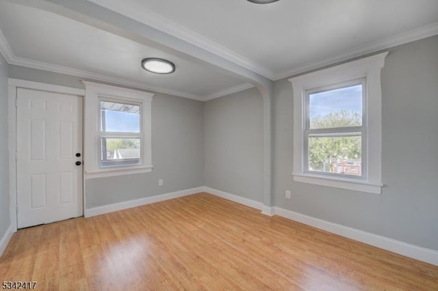 spare room featuring light wood-type flooring, plenty of natural light, ornamental molding, and baseboards