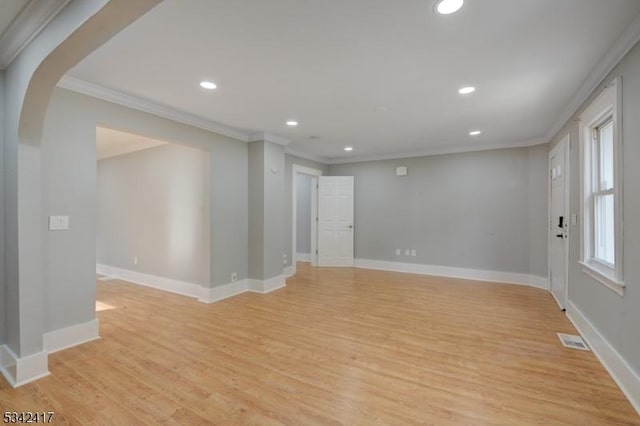 empty room featuring light wood-type flooring, baseboards, arched walkways, and ornamental molding