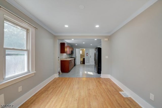 unfurnished living room featuring ornamental molding, light wood-style floors, visible vents, and baseboards