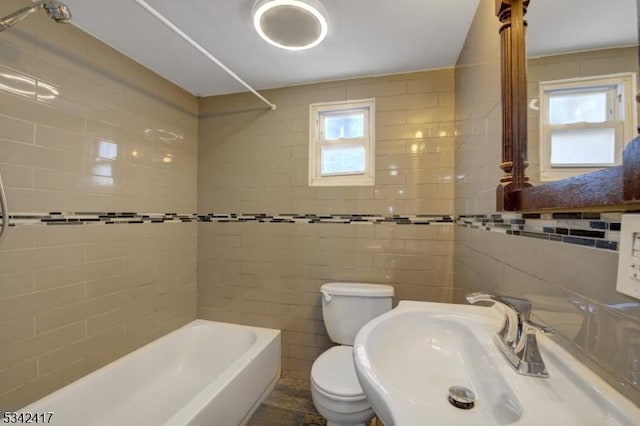 bathroom with toilet, bathtub / shower combination, a sink, and tile walls