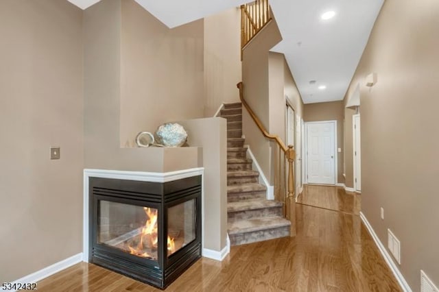 staircase with visible vents, baseboards, wood finished floors, a multi sided fireplace, and recessed lighting