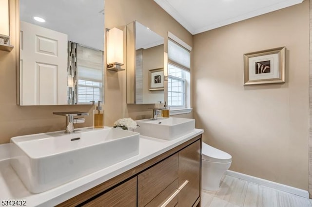 bathroom with toilet, crown molding, baseboards, and a sink