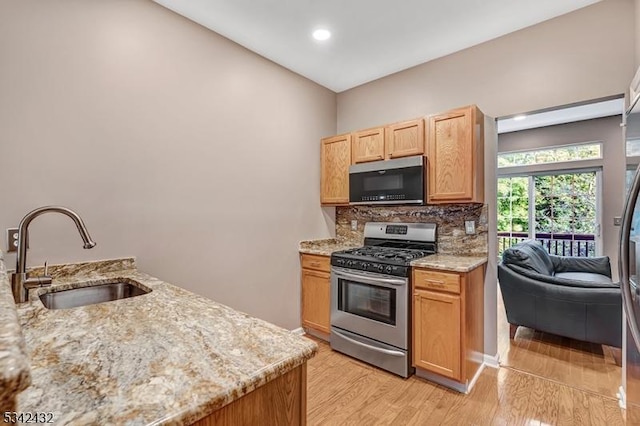 kitchen featuring light wood-style flooring, stainless steel appliances, a sink, light stone countertops, and tasteful backsplash