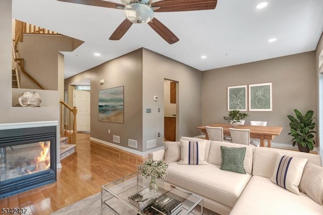 living room featuring light wood-style floors, a glass covered fireplace, visible vents, and baseboards