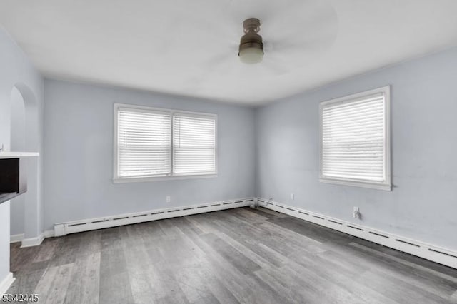 unfurnished room featuring a baseboard heating unit, a ceiling fan, arched walkways, and wood finished floors