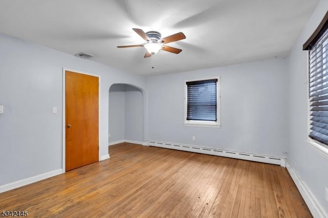 empty room with arched walkways, visible vents, baseboards, baseboard heating, and hardwood / wood-style floors