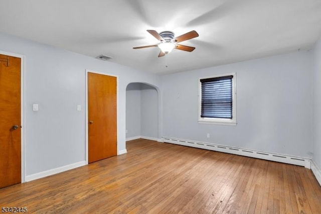 unfurnished room with arched walkways, visible vents, a ceiling fan, baseboard heating, and wood-type flooring