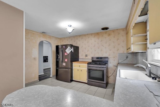 kitchen featuring arched walkways, light tile patterned floors, stainless steel appliances, a sink, and wallpapered walls