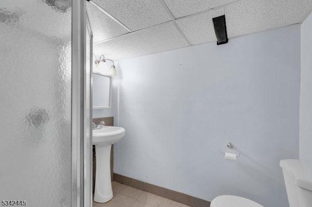 bathroom featuring a drop ceiling, toilet, a sink, baseboards, and tile patterned floors