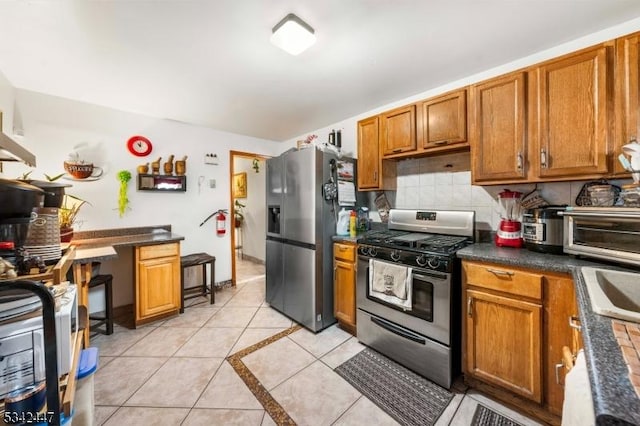 kitchen with light tile patterned floors, appliances with stainless steel finishes, brown cabinetry, and backsplash