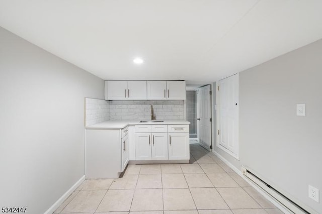 kitchen featuring decorative backsplash, white cabinets, baseboard heating, light countertops, and a sink