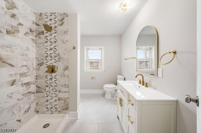 bathroom with toilet, a tile shower, vanity, and baseboards