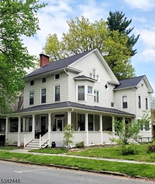 view of front facade featuring a front yard, covered porch, and a chimney