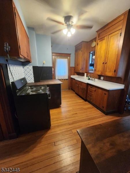 kitchen with tasteful backsplash, electric range, light wood-style floors, brown cabinetry, and a sink