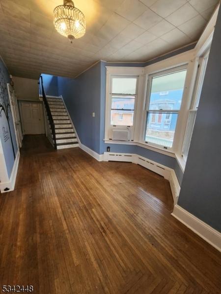 unfurnished living room with cooling unit, baseboards, stairway, and dark wood-style flooring