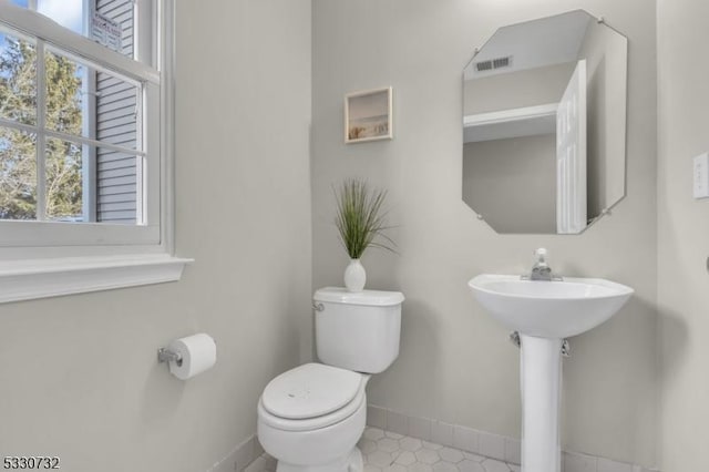 half bathroom with toilet, baseboards, visible vents, and a sink